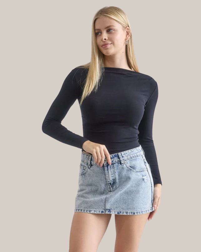 Woman wearing a black long-sleeve top and denim skirt on a beige background