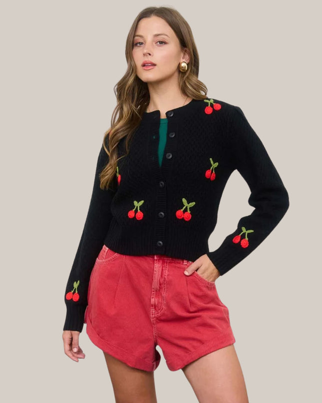 Woman wearing a black sweater with cherry designs and red shorts on a beige background