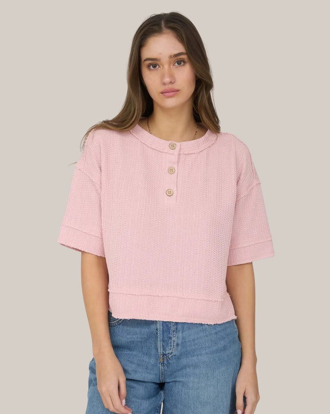 Woman wearing a pink short-sleeve top and blue jeans on a plain background