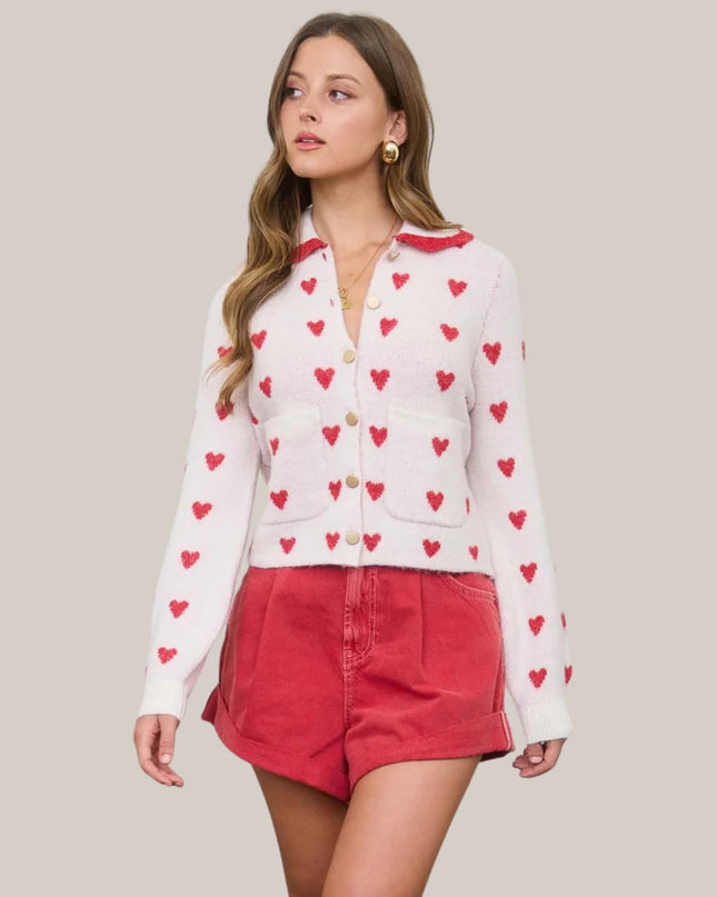 Woman wearing a white cardigan with red heart patterns and red shorts on a beige background