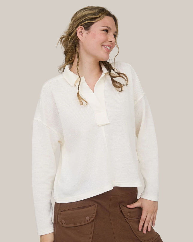 Woman wearing a white blouse and brown pants against a plain background