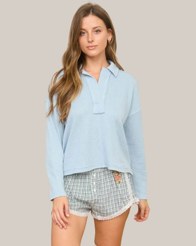 Woman wearing a light blue shirt and plaid shorts on a plain background