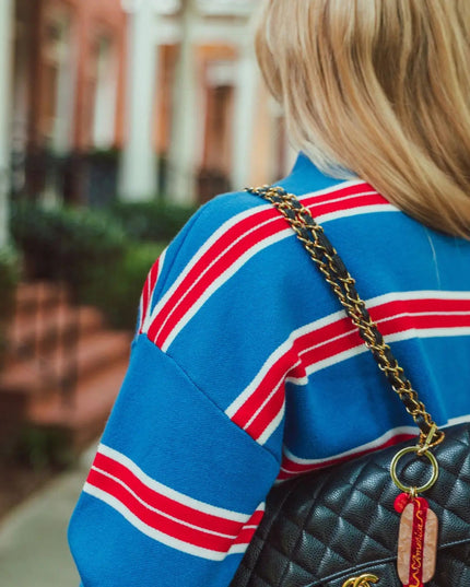 A woman from behind wearing a blue sweater with red and white stripes, carrying a black quilted Chanel shoulder bag with a gold chain strap.