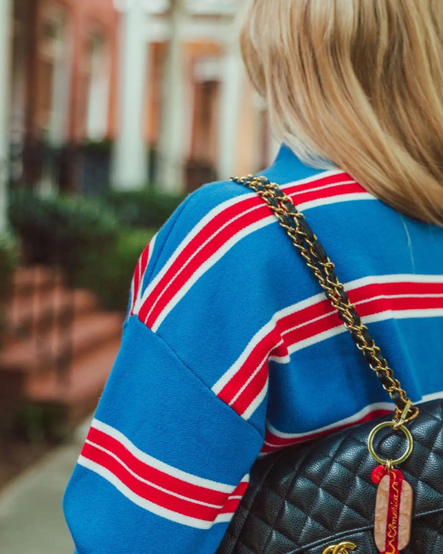 A woman from behind wearing a blue sweater with red and white stripes, carrying a black quilted Chanel shoulder bag with a gold chain strap.
