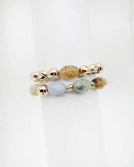 Two beaded stretch bracelets stacked on a white background. The top bracelet features metallic gold beads with a central brown stone, and the bottom bracelet features metallic gold beads with a light blue stone and a green stone.