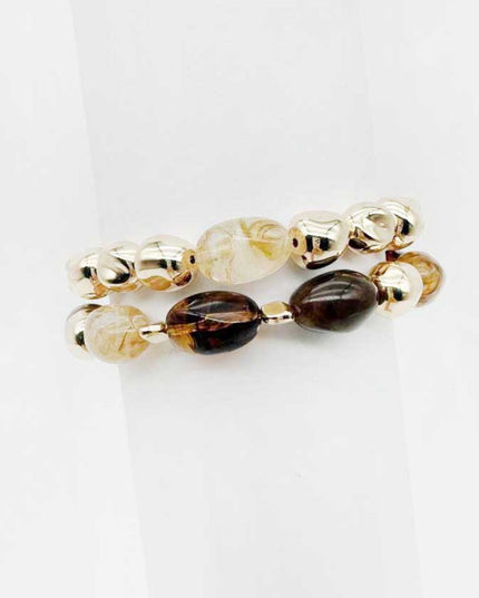 A pair of beaded stretch bracelets on a white background. One bracelet features metallic gold-toned beads, and the other features smooth translucent beads in cream, smoky brown, and dark brown.