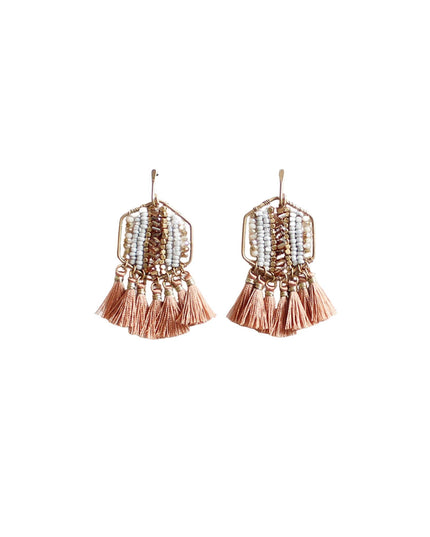 A pair of bohemian-style geometric dangle earrings in rose gold and white, featuring a hexagonal frame with white beads and dangling rose gold tassels, shown on a plain white background.