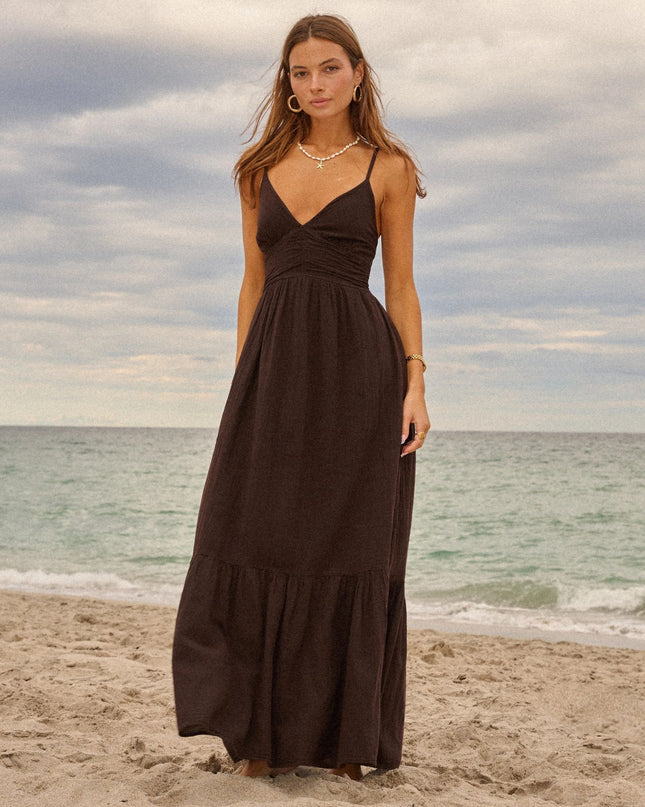 Woman in a black dress standing on a beach with ocean and cloudy sky in the background