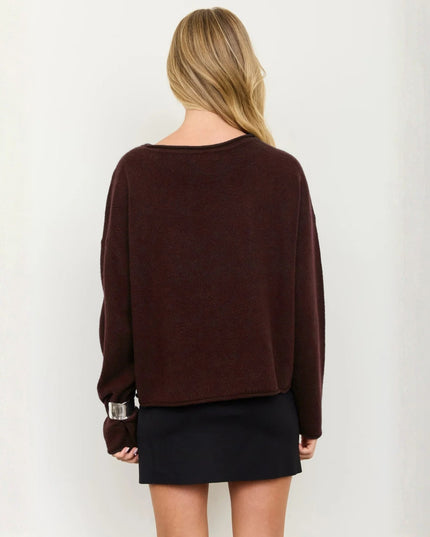 A woman shown from the back wearing a dark brown knit sweater and a black mini skirt against a plain off-white background.