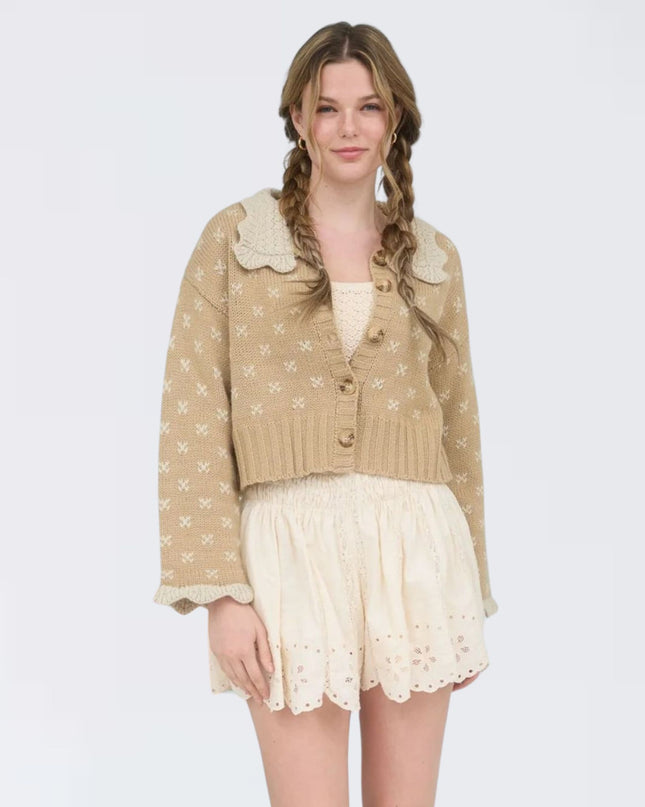 Woman wearing a beige cardigan with lace details and a white skirt on a light gray background