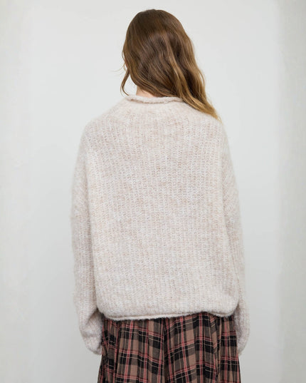 A woman viewed from behind wearing a fuzzy, textured knit sweater in a light cream-beige color, paired with a red and black plaid skirt, against a plain light gray background.