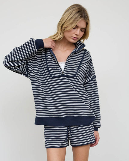A woman modeling a matching navy and white striped lounge set, featuring a long-sleeve half-zip pullover and coordinating shorts, against a plain light gray studio background.