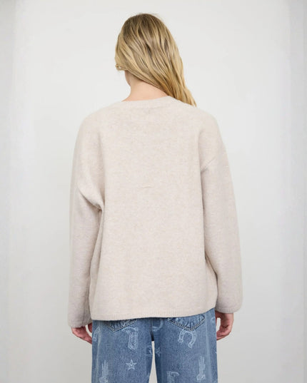 A woman viewed from behind wearing a light beige knit sweater and blue jeans against a plain light gray background.