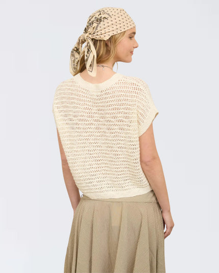 Woman wearing a beige knitted top and skirt with a matching headscarf on a light gray background