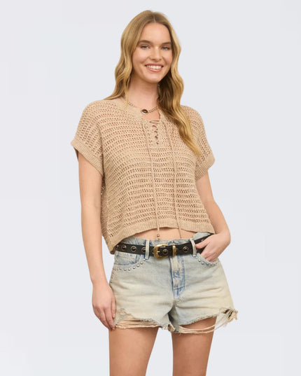 Woman wearing a beige crochet top and denim shorts on a plain background