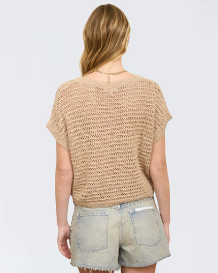 Woman wearing a beige crochet top and denim shorts on a white background