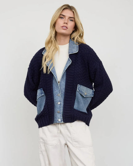 A blonde model wearing a navy blue knit cardigan with light blue denim patch pockets and a denim placket, styled with a white t-shirt and off-white cargo pants against a plain light gray background.