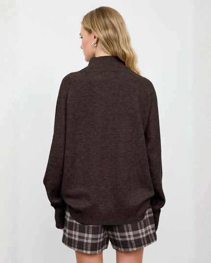 A woman shown from the back wearing a dark brown knit mock-neck sweater and plaid shorts against a plain white background.