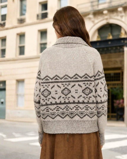 A woman viewed from behind wearing a cream-colored knit sweater with a dark gray geometric Fair Isle pattern, standing on a city street in front of a beige building.