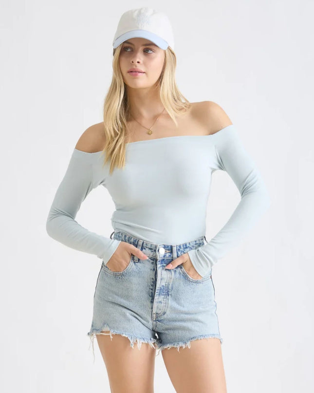 Woman wearing a light gray off-shoulder top and denim shorts on a white background