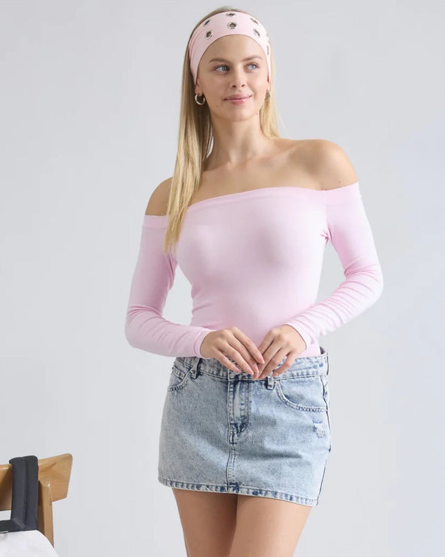 Woman wearing a pink off-shoulder top and denim skirt on a plain background