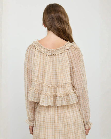A woman viewed from behind wearing a beige and white gingham long-sleeve top with ruffled trim and a matching skirt against a light neutral background.