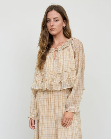 A woman modeling a beige and white gingham two-piece set consisting of a long-sleeve ruffled top and matching skirt, against a plain light gray background.