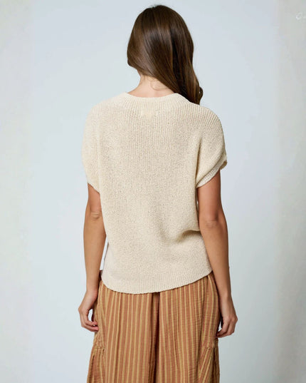A woman shown from the back wearing a short-sleeve cream knit top and brown striped pants against a plain light gray background.