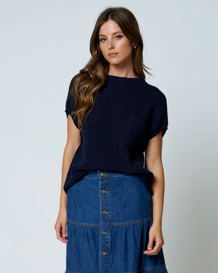 A woman modeling a dark navy blue short-sleeve knit top paired with a blue denim tiered skirt, standing against a light gray studio background.