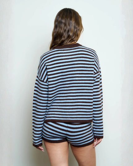 A woman viewed from behind wearing a matching striped knit top and shorts set in dark brown and light blue, standing against a plain off-white wall.