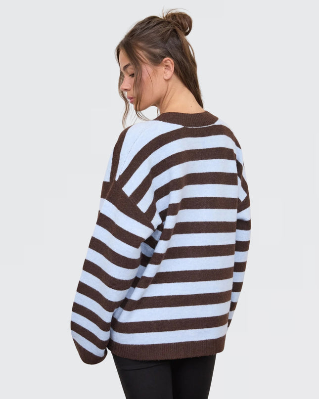 A woman wearing a brown and white striped knit sweater, shown from a side-back angle against a light gray studio background.