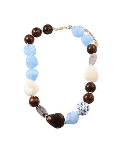 A beaded necklace featuring light blue, dark brown, cream, and gray beads, with a small blue and white patterned accent bead and a gold-tone clasp, shown on a plain white background.