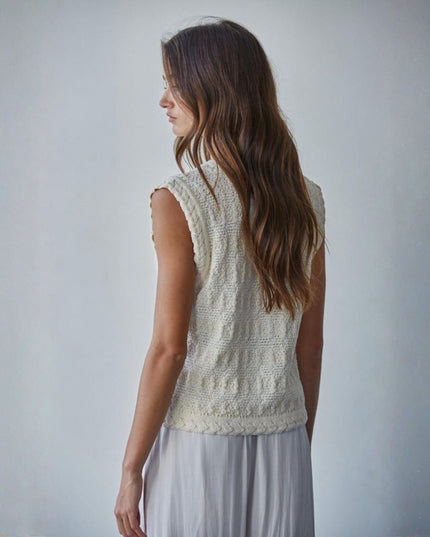Woman wearing a light-colored sleeveless knitted top against a plain background