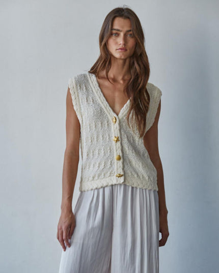 Woman wearing a sleeveless knitted cardigan with gold buttons against a plain background