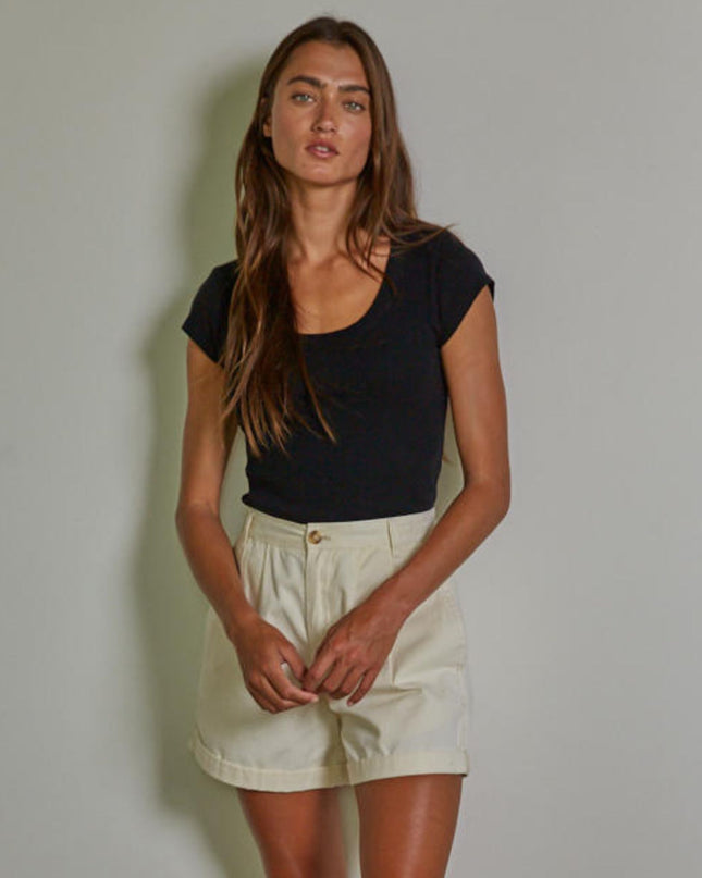 Woman wearing a black top and beige shorts against a plain background