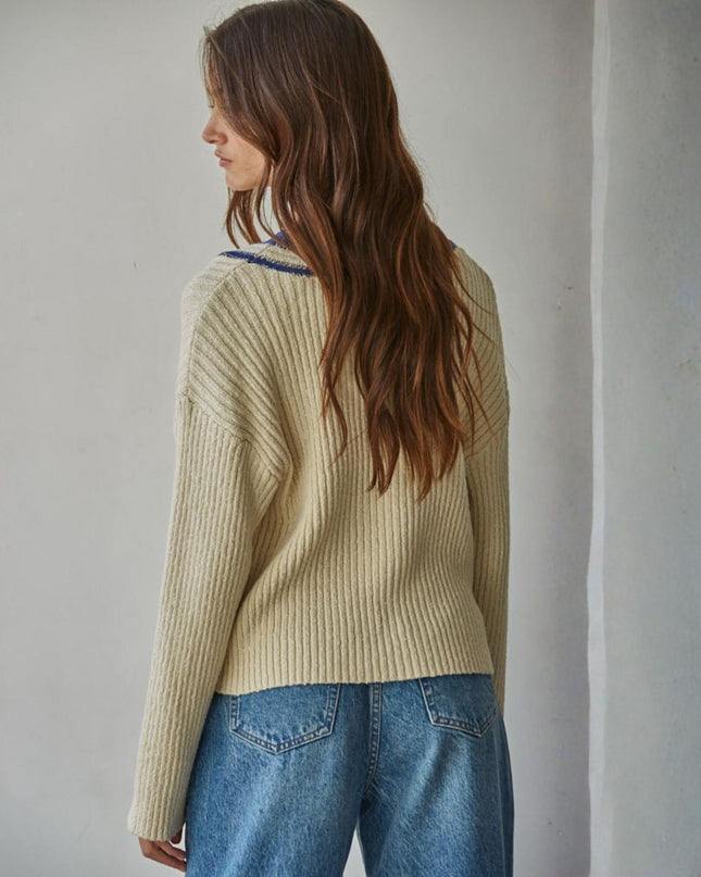 Woman wearing a beige sweater and blue jeans against a plain wall