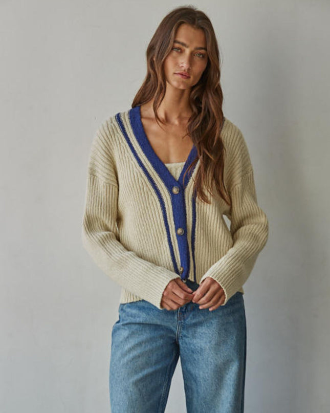 Woman wearing a beige cardigan with blue trim and blue jeans against a plain background