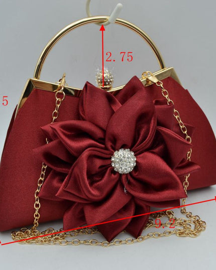 A burgundy satin evening handbag with a large flower applique and gold-tone chain details, shown with red dimension lines and measurements on a light gray background.