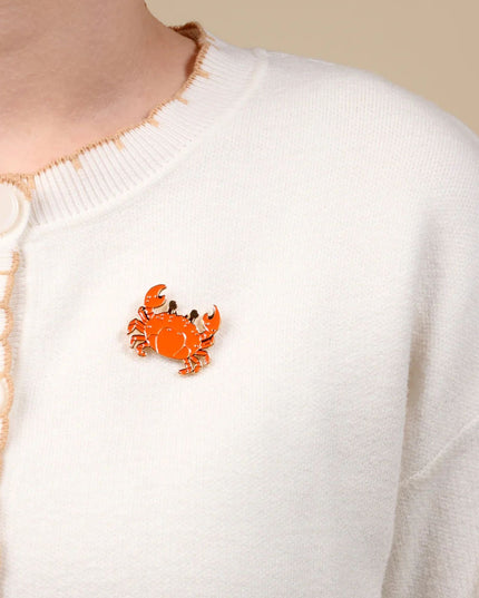 Orange crab brooch on a white sweater with button details