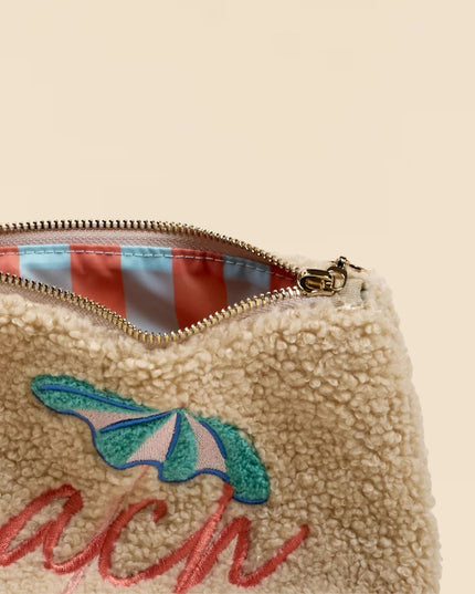 Beige pouch with 'beach' embroidery and striped interior on a beige background