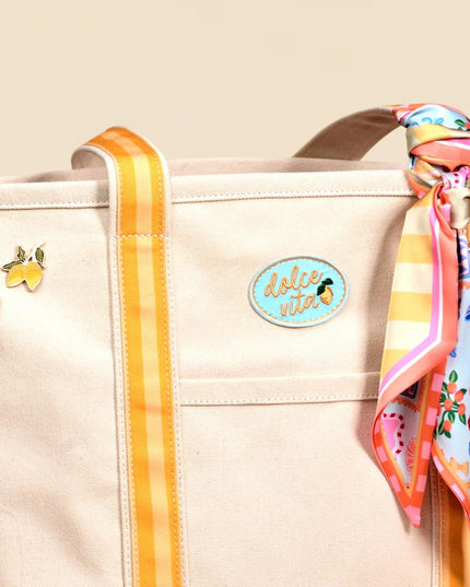 Beige tote bag with colorful ribbon, earrings, and decorative patch on a beige background