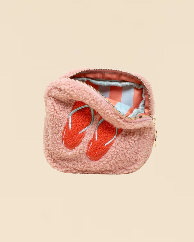 Pink fuzzy pouch with red flip-flops inside on a beige background