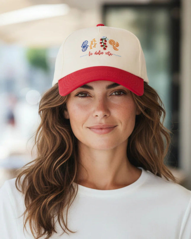 Woman wearing a beige and red cap with colorful designs and text.