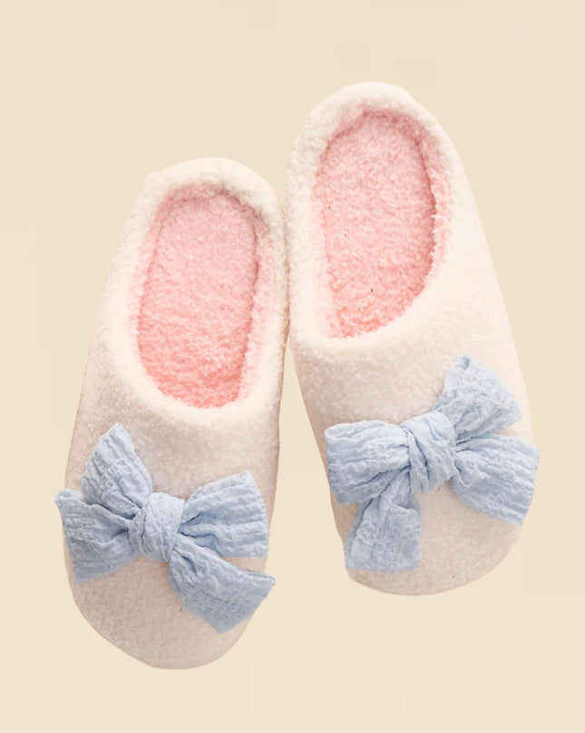 Pair of slippers with pink interior and blue bows on a beige background