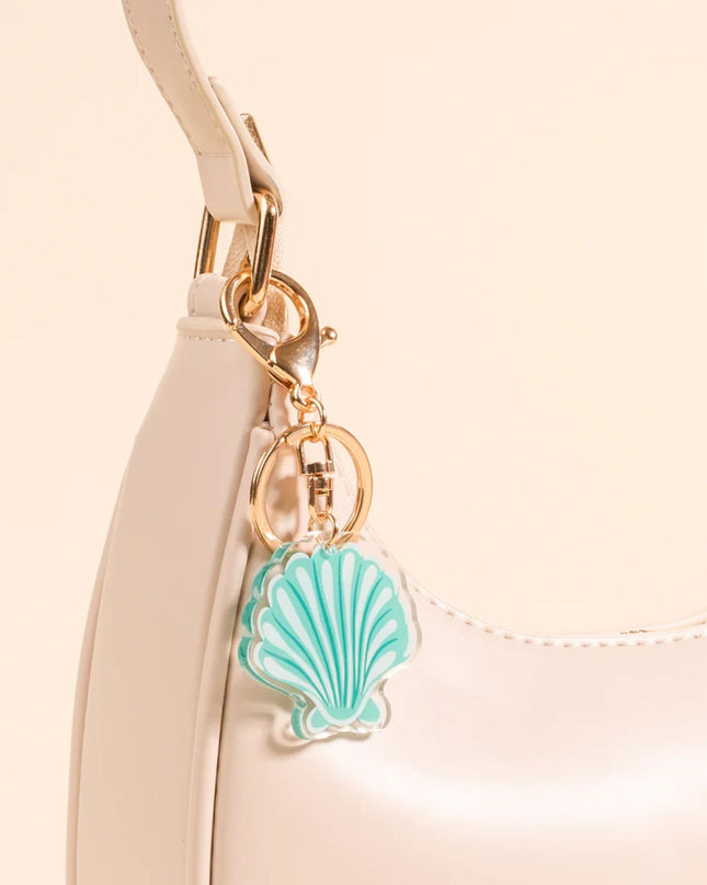 Beige handbag with a turquoise shell charm on a beige background