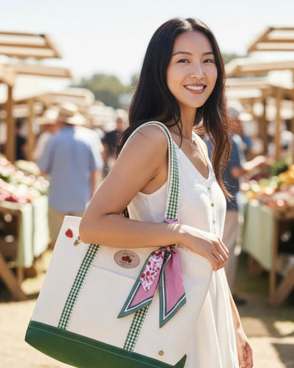 Woman holding a white tote bag with green accents at an outdoor market.