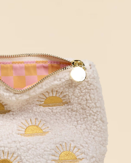 White pouch with gold sun designs and a pink and orange checkered zipper on a beige background