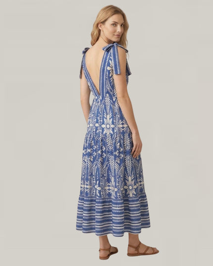 A woman modeling a blue and white patterned maxi dress with a tie-shoulder back, shown from the back against a solid light gray background.