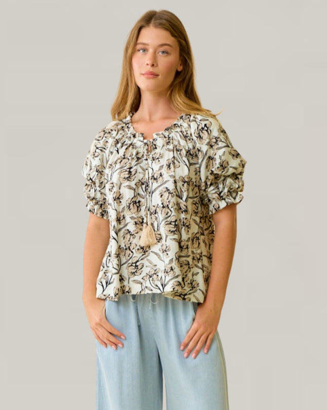 Woman wearing a floral blouse and light blue pants against a plain background