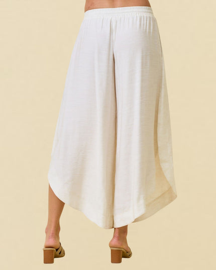 White wide-leg cropped pants shown from the back on a model, paired with tan block-heel slide sandals against a solid beige background.